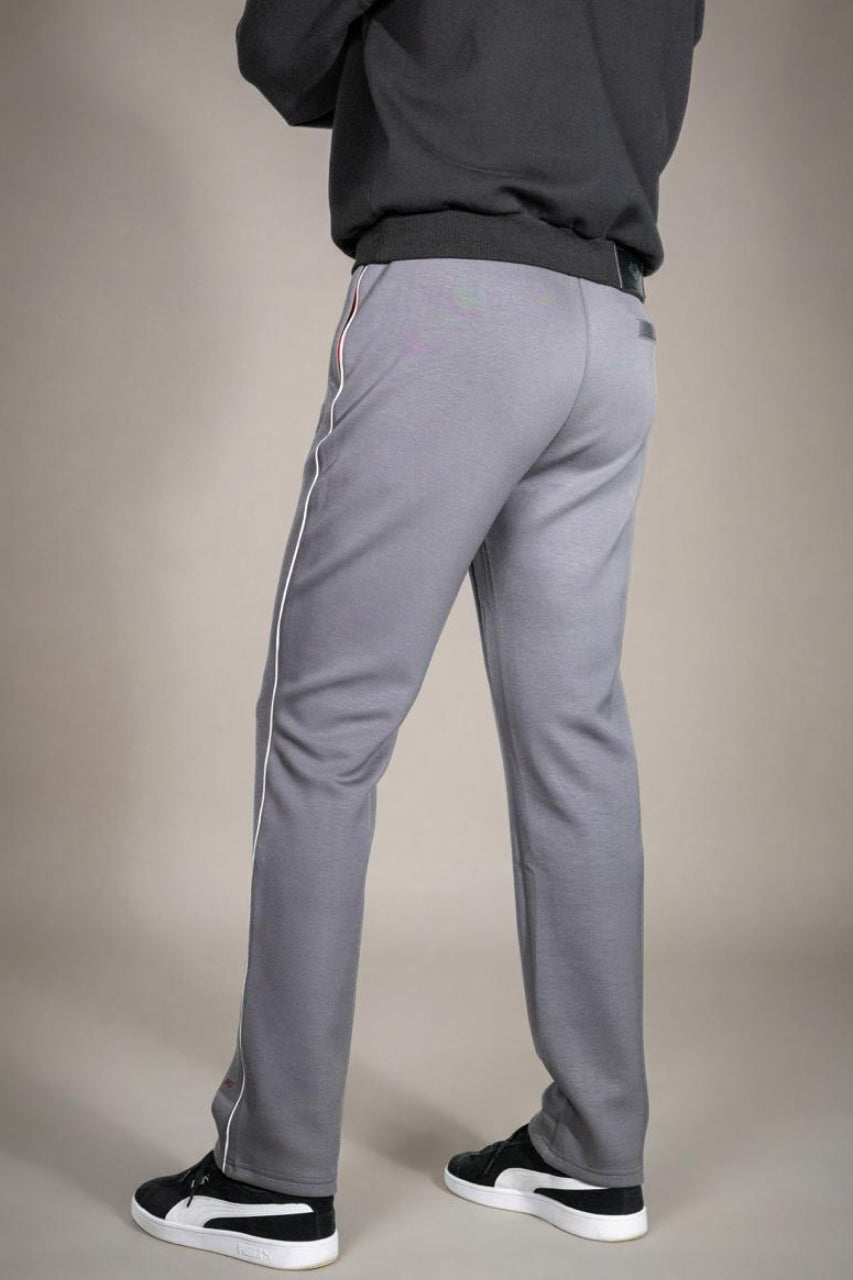 Achteraanzicht van de grijze heren joggingbroek, gedragen door een model, met focus op de pasvorm van de billen, de elastische tailleband en de doorlopende witte zijstreep. Tegen een effen beige achtergrond.