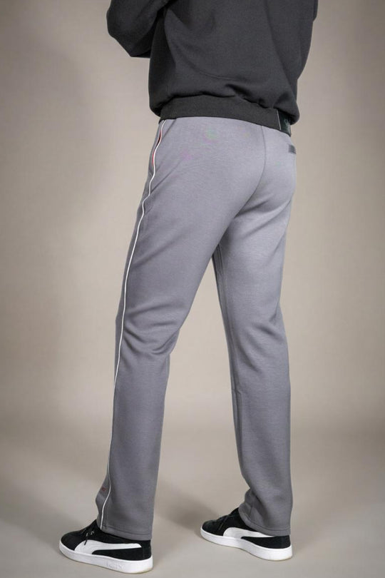 Achteraanzicht van de grijze heren joggingbroek, gedragen door een model, met focus op de pasvorm van de billen, de elastische tailleband en de doorlopende witte zijstreep. Tegen een effen beige achtergrond.