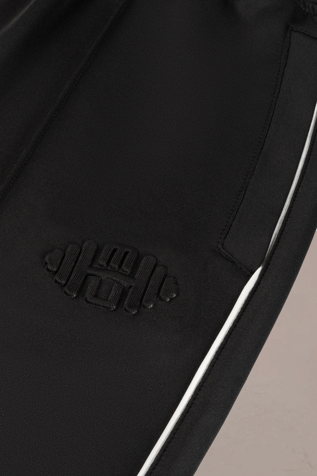 Detailshot van embossed halterlogo op zwarte heren sportbroek, close-up van hoogwaardig materiaal en textuur