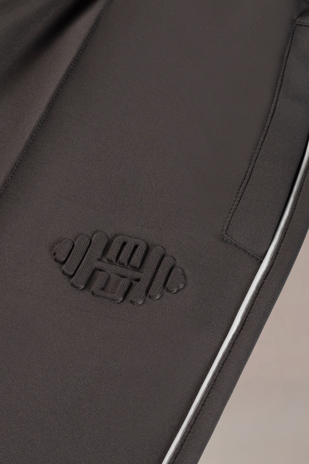 Detailshot van embossed halterlogo op grijze heren sportbroek, close-up van hoogwaardig materiaal en textuur