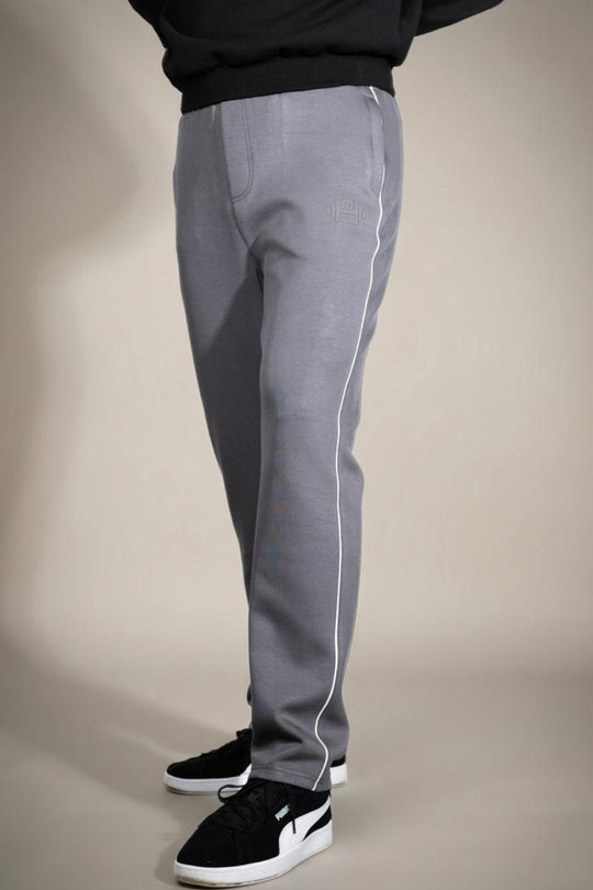 zij-aanzicht van een model dat een grijze joggingbroek voor heren draagt met een witte zijstreep, een subtiel logo op het bovenbeen en zwarte sneakers.