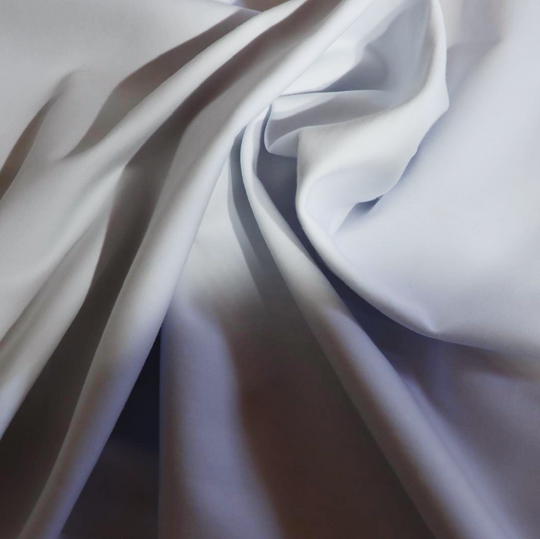 Close-up van de zachte, hoogwaardige stof van een witte oversized T-shirt, waarbij de natuurlijke plooien en gladde textuur duidelijk zichtbaar zijn.