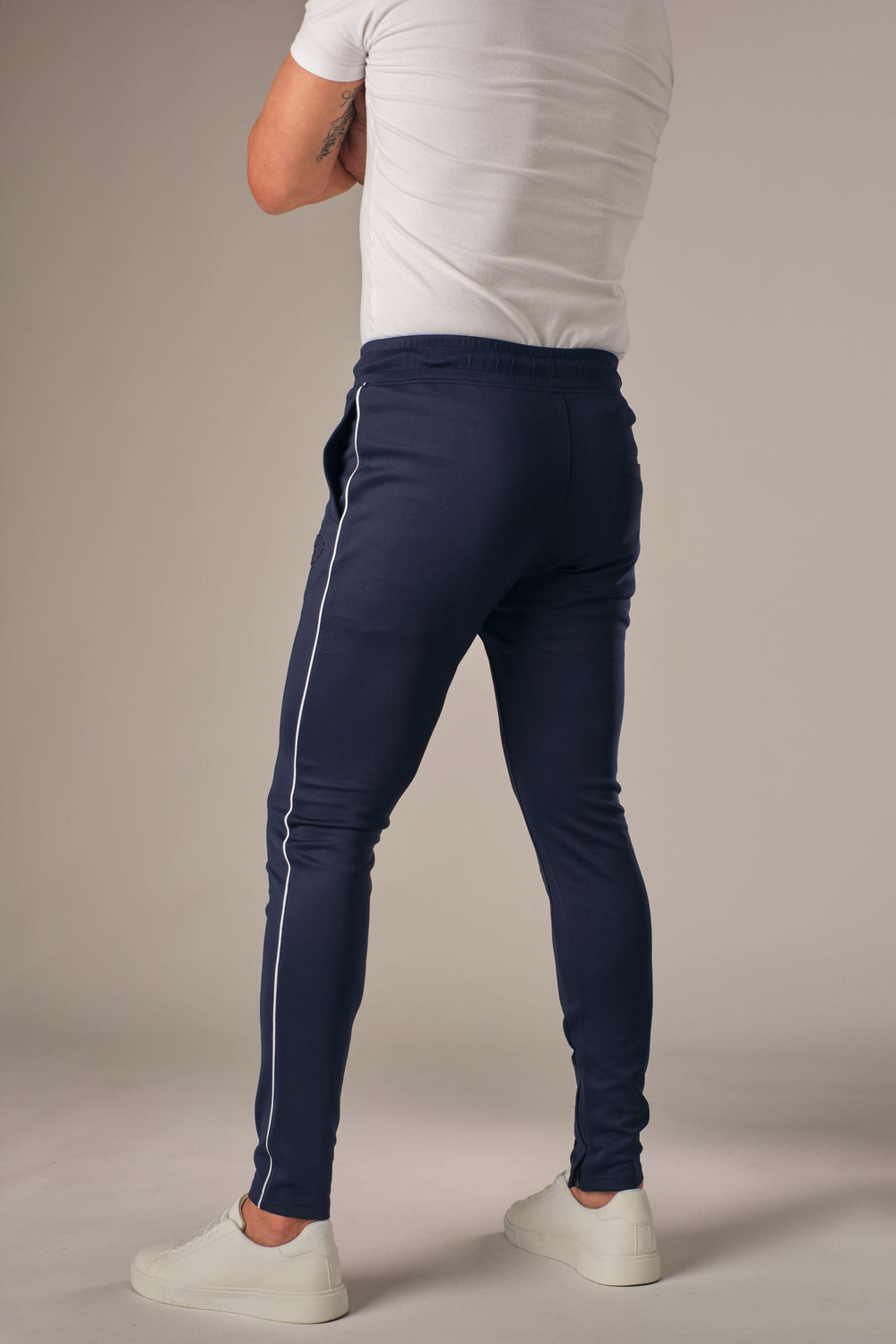 Blauwe muscle fit sportbroek voor heren met witte zijstreep, achterkant full body weergave, gedragen met wit T-shirt en witte sneakers