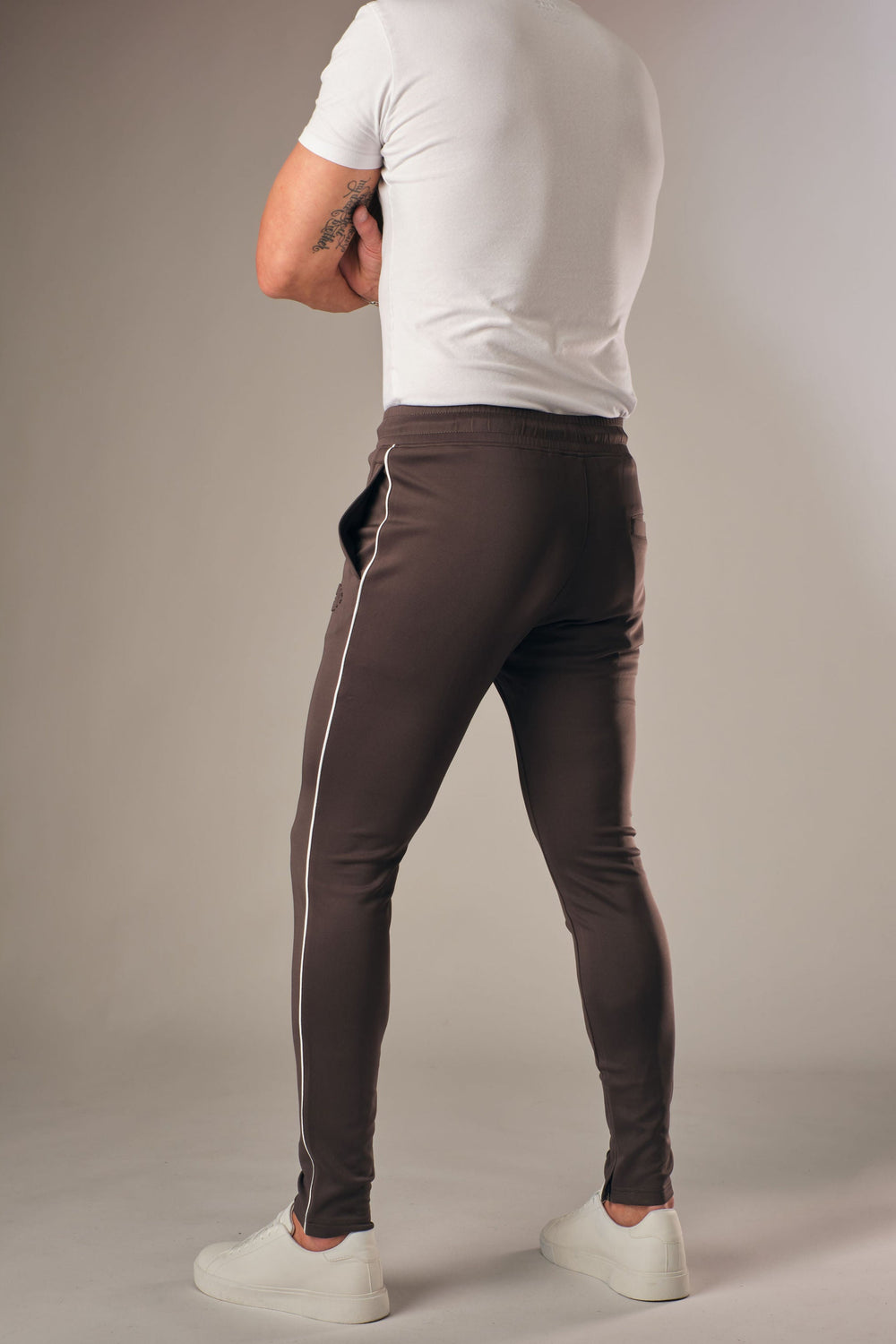 Grijze muscle fit sportbroek voor heren met witte zijstreep, achterkant full body weergave, gedragen met wit T-shirt en witte sneakers