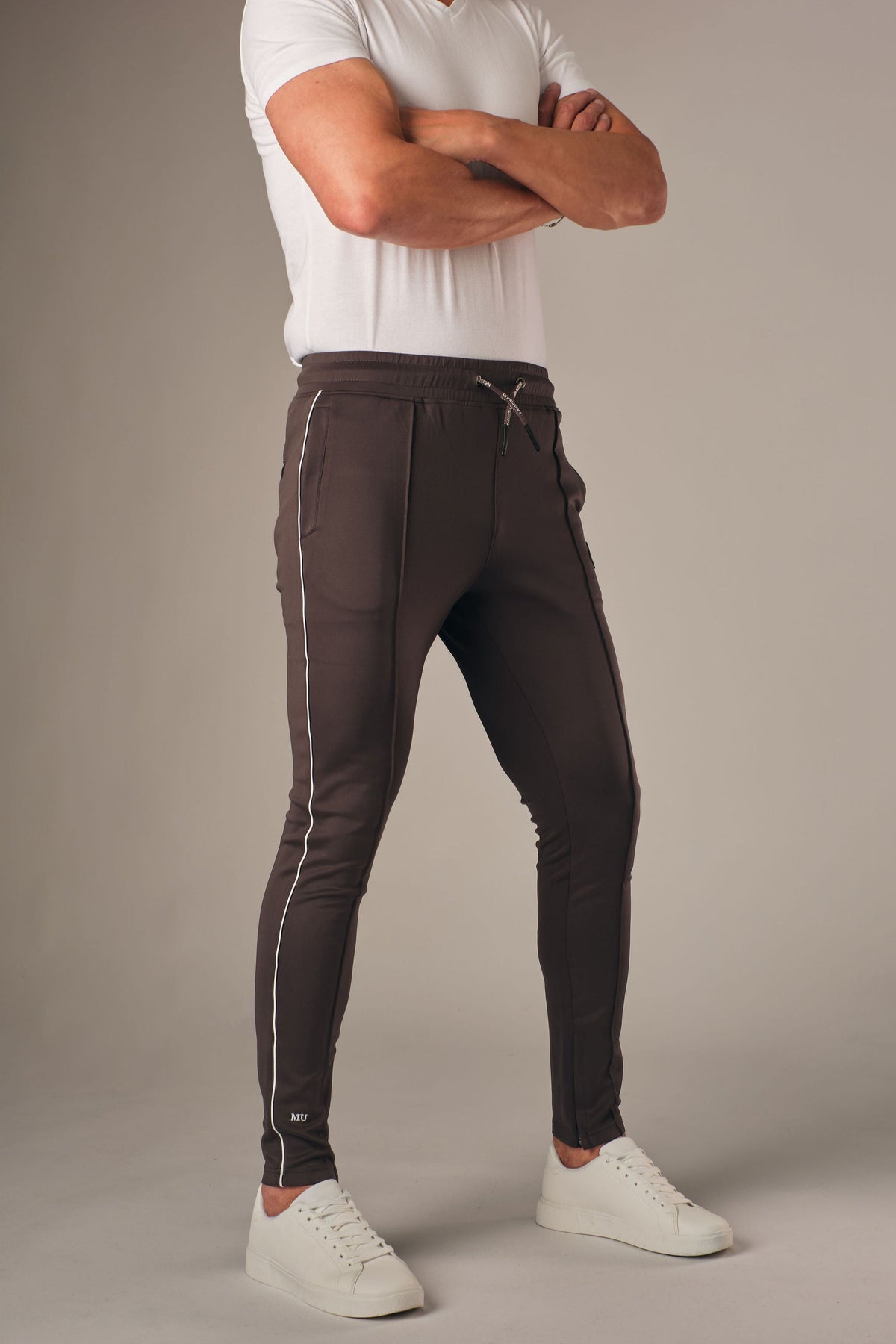Grijze muscle fit sportbroek voor heren met witte zijstreep en embossed halterlogo, full body vooraanzicht, gedragen met wit T-shirt en witte sneakers