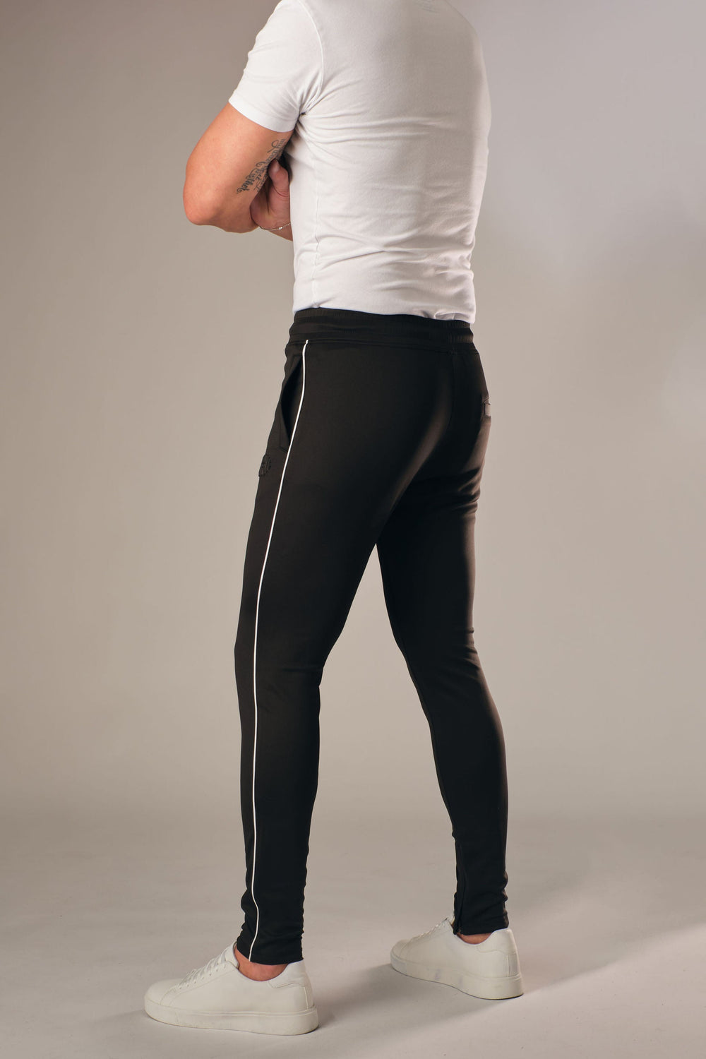 Zwarte muscle fit sportbroek voor heren met witte zijstreep, achterkant full body weergave, gedragen met wit T-shirt en witte sneakers