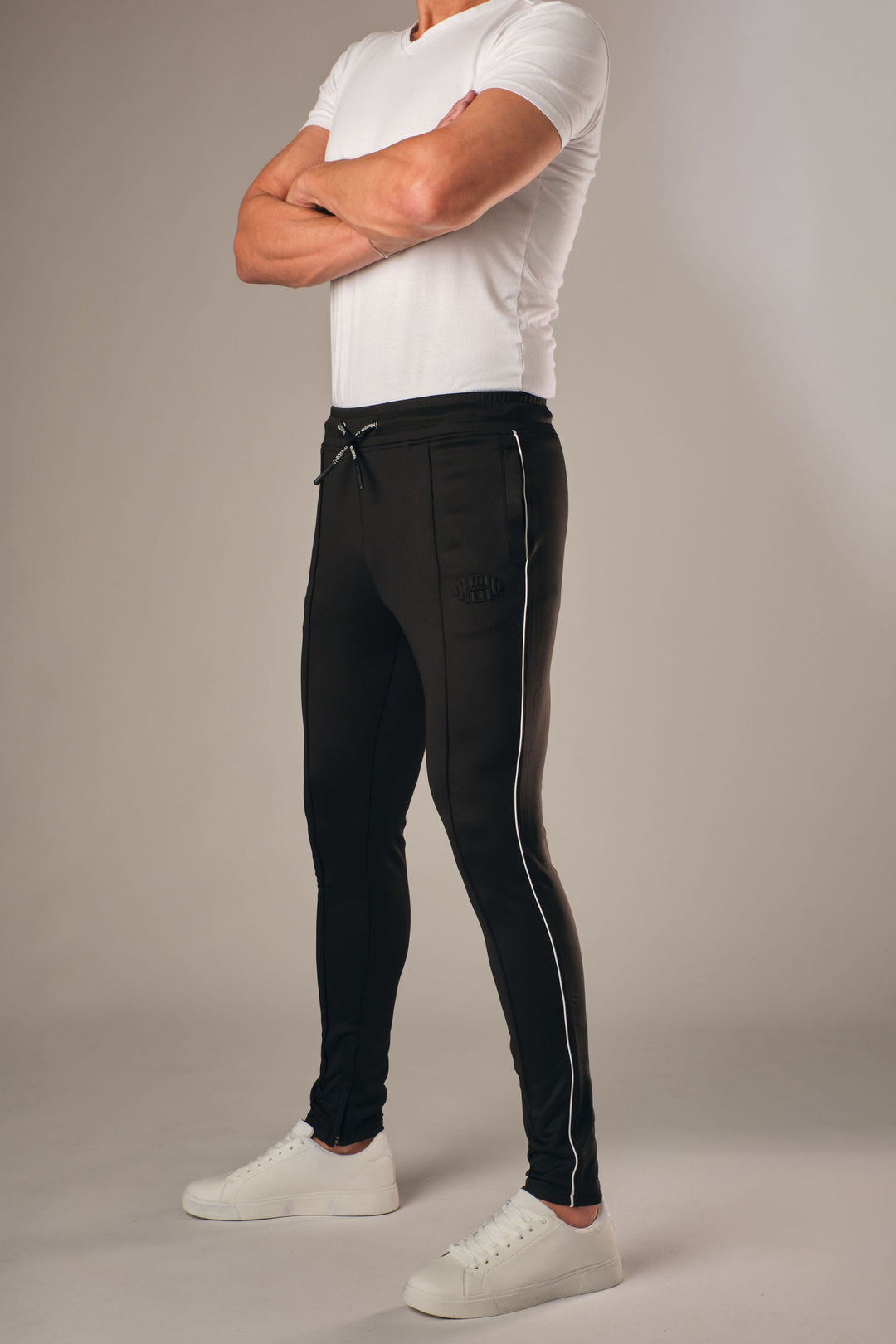 Zwarte muscle fit sportbroek voor heren met witte zijstreep en embossed halterlogo, full body vooraanzicht, gedragen met wit T-shirt en witte sneakers