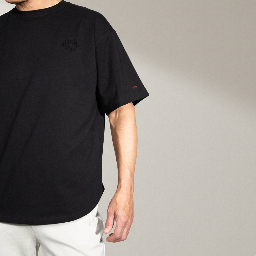 voorkant van het zwarte oversized T-shirt, gedragen door een mannelijk model. De foto toont de ronde zoomlijn en de losse, comfortabele pasvorm. De effen zwarte stof benadrukt de premium kwaliteit en het minimalistische ontwerp. Ideaal voor een casual en luxe uitstraling.