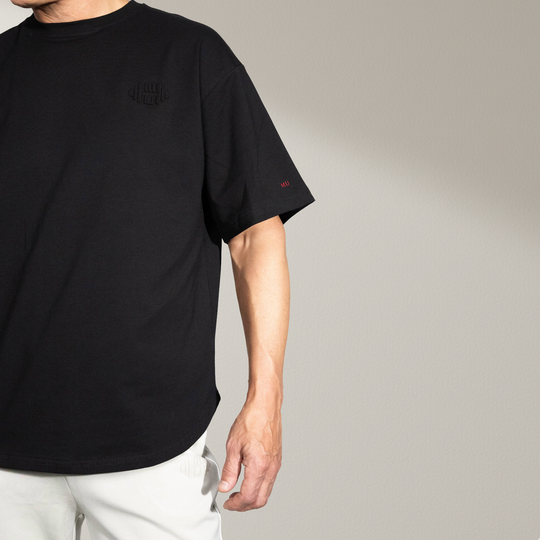 voorkant van het zwarte oversized T-shirt, gedragen door een mannelijk model. De foto toont de ronde zoomlijn en de losse, comfortabele pasvorm. De effen zwarte stof benadrukt de premium kwaliteit en het minimalistische ontwerp. Ideaal voor een casual en luxe uitstraling.