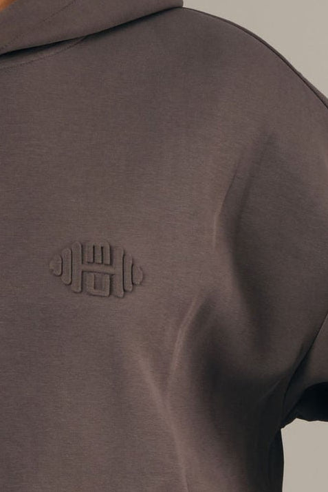 Close-up van de hoogwaardige grijze stof van een dameshoodie, voorzien van een verfijnd embossed logo.